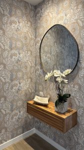 Papel pintado floral tonos tierra en recibidor de Amara con repisa de madera y espejo redondo