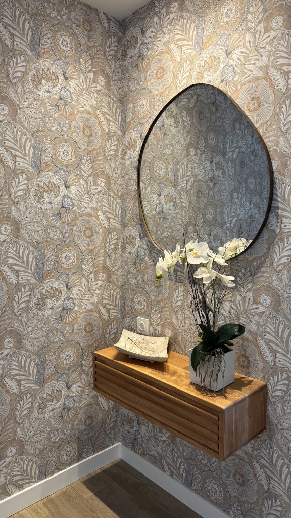 Papel pintado floral tonos tierra en recibidor de Amara con repisa de madera y espejo redondo